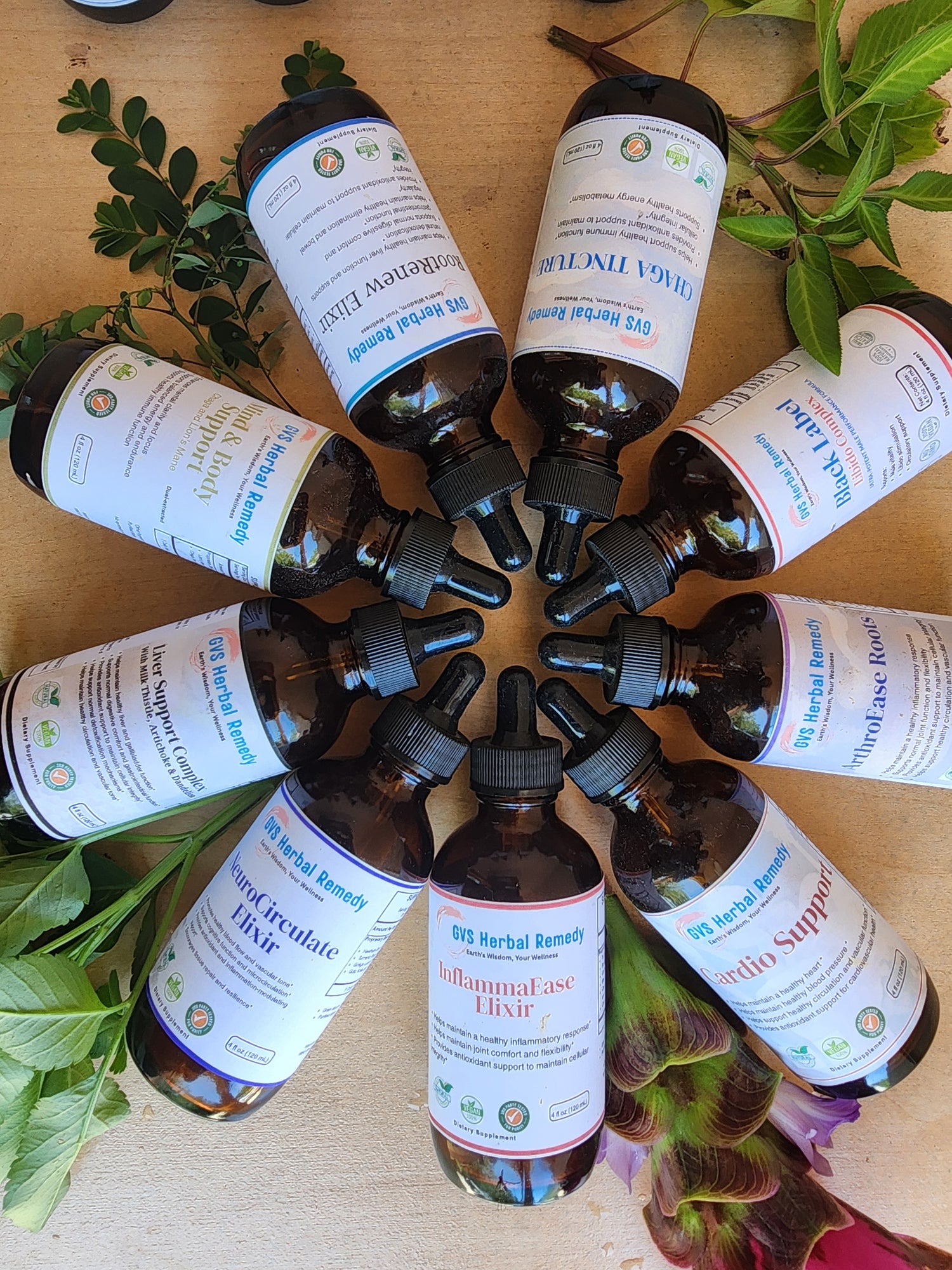 Collection of herbal tincture bottles with droppers on a wooden surface surrounded by green leaves.